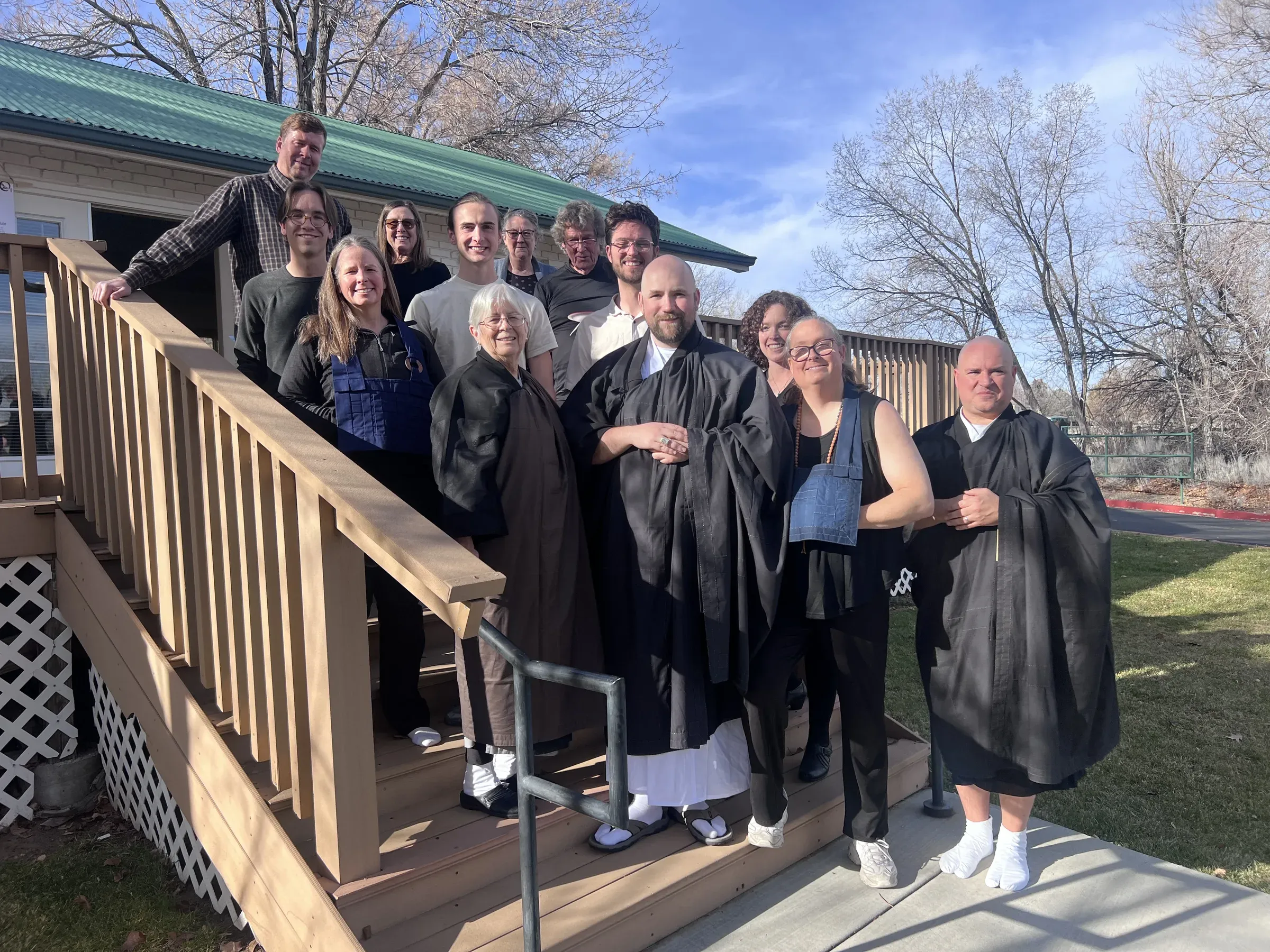 Rev. Shinzan Sekibu Alice Tulloch, Sōbu Tetsuzan Jeff Urmston, Ungan Jiyu, and other members of the sangha standing together outside after the shukke tokudo/jukai ceremony, smiling at the camera.