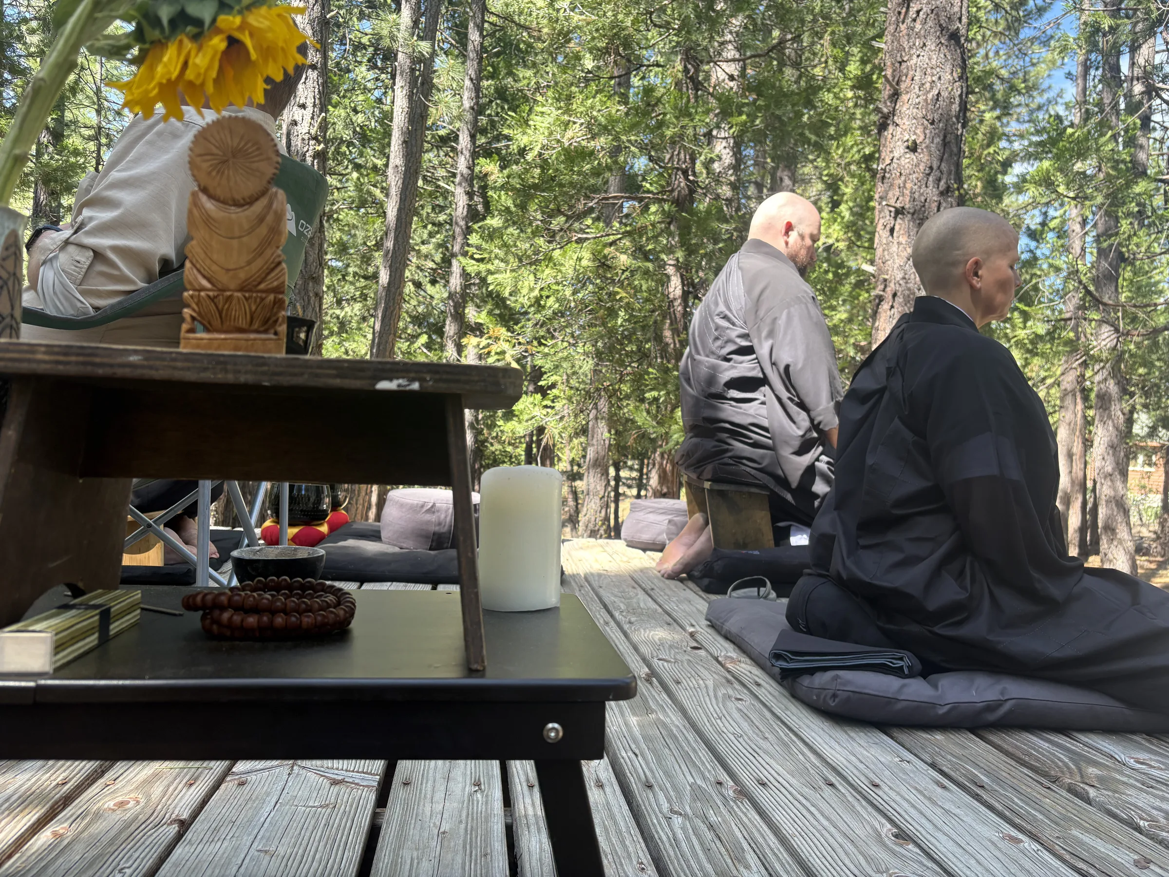 Kate and Noel sitting on a platform in the forest with a small altar with Kannon statue in the foreground.