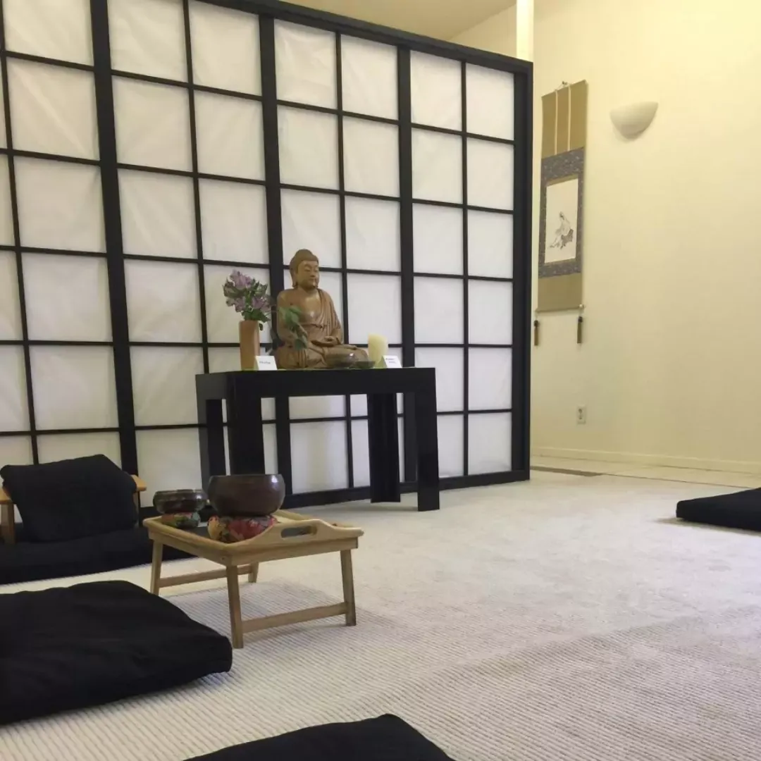Bodhi Oak Zendo with small Buddha statue in front of shoji screen with cushions and bells in foreground.
