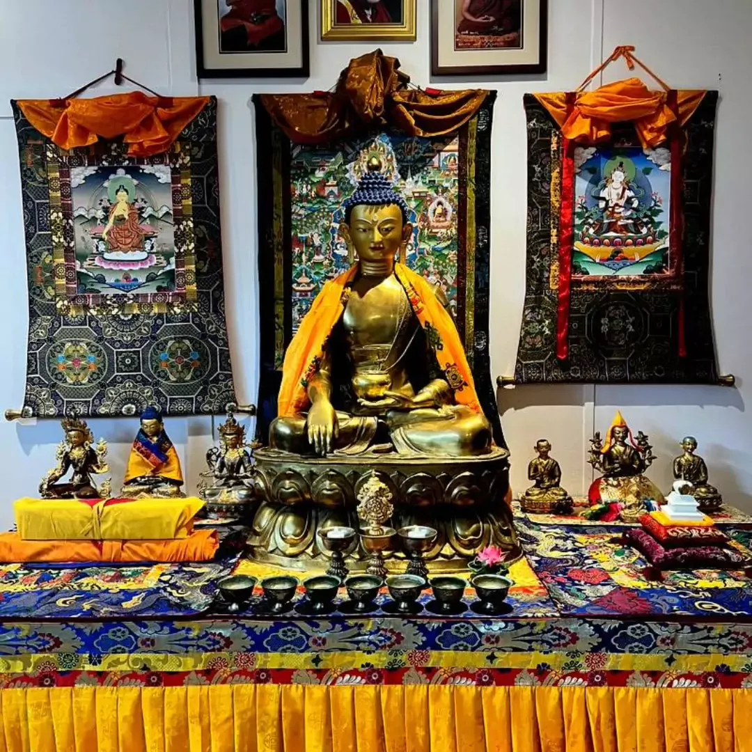 Alter with large golden statue of the Buddha, surrounded by Tibetan imagery, with candles and offerings.