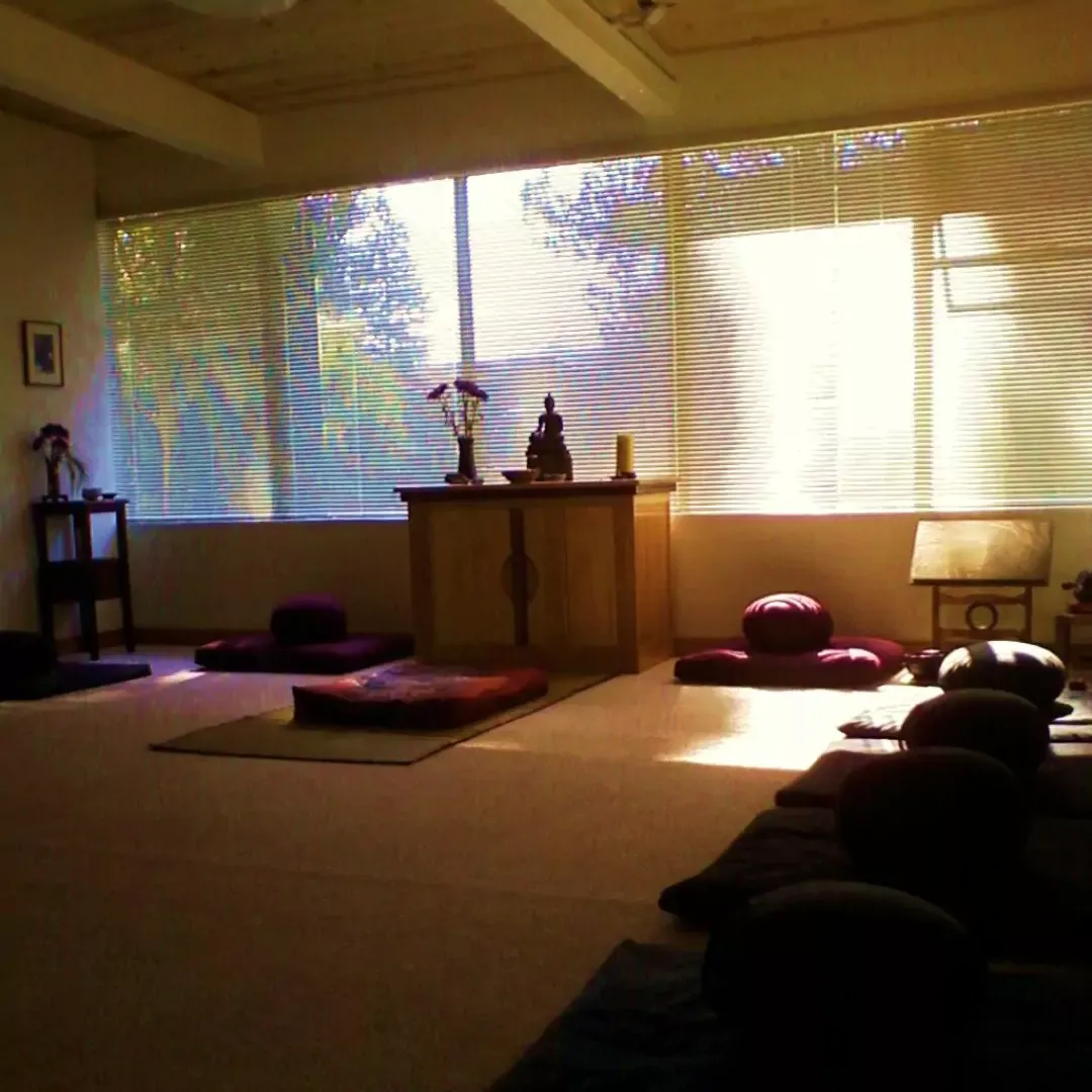 Mt. Diablo zendo with small Buddha statue on alter with candle and flowers, surrounded by zabutons and zafus.
