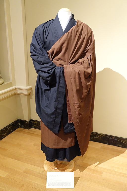 A brown okesa robe draped on a mannequin wearing black and white Japanese koromo and kimono.
